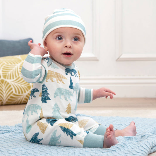 Baby wearing a onesie with bear patterns and a striped hat, sitting on a blue blanket.
